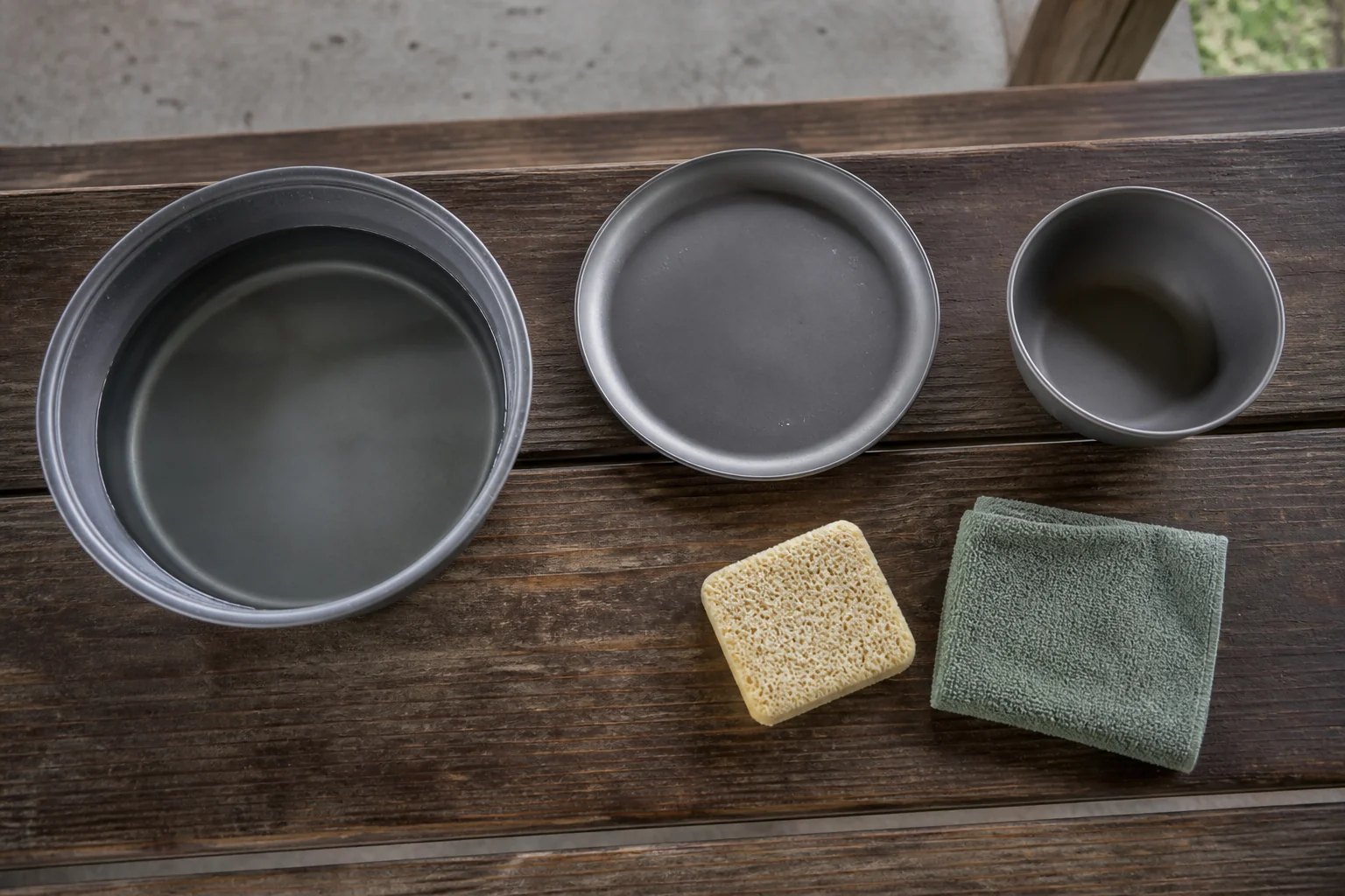 Anodized aluminum camping tableware with gentle cleaning tools at an outdoor wash station