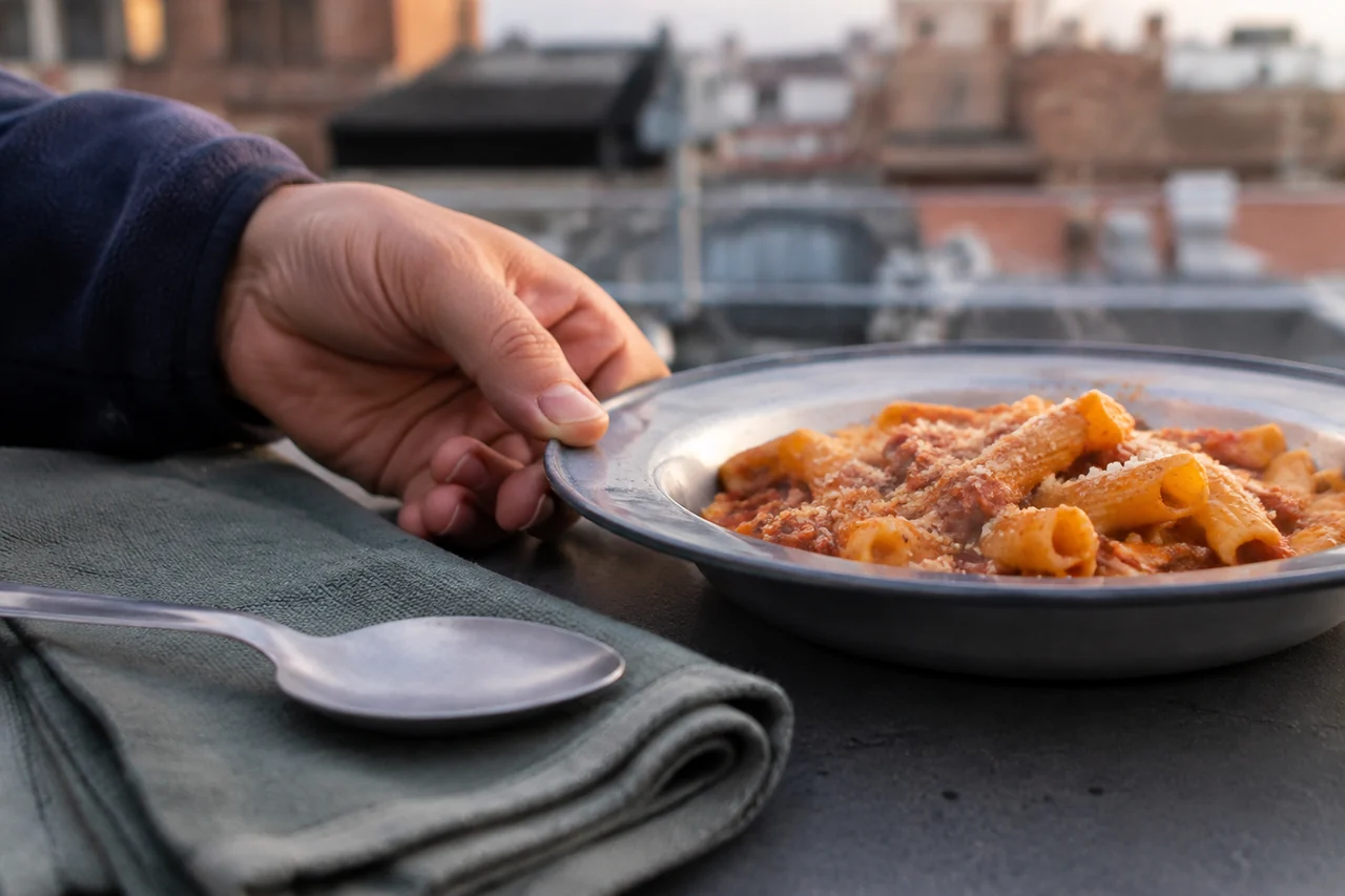 Hand holding the rim of a camping plate containing hot pasta