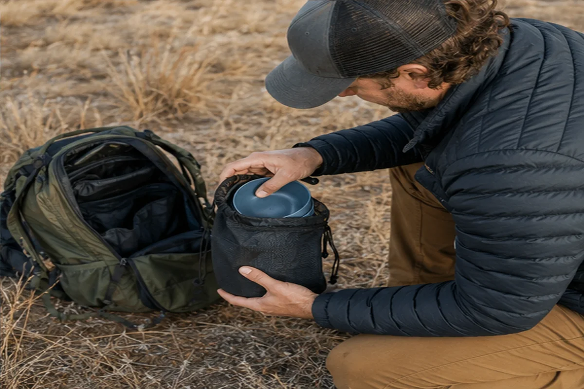 One-Person Camping Set Pack-Out One-person camping dinnerware set packed beside a backpack on dry grassland
